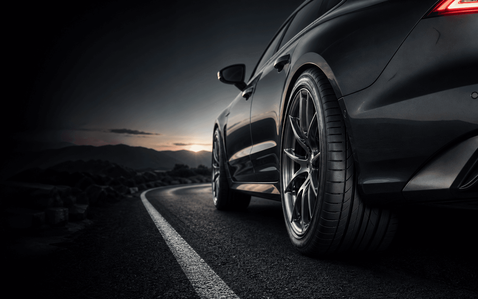 Performance tire on a dark sports sedan on a mountain road